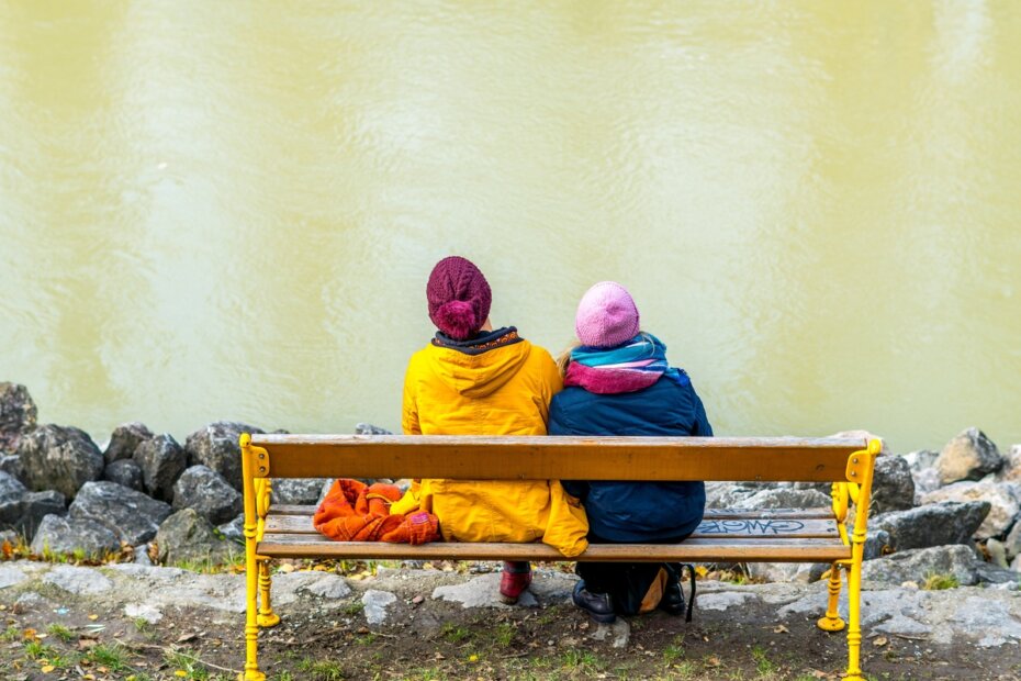 couple people colorful clothes sitting wooden yellow bench facing white wall 1 1